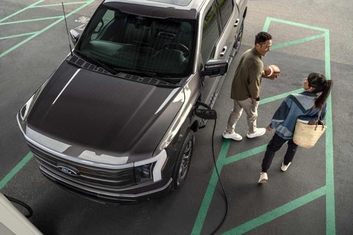 Overhead shot of a couple walking away from a 2024 Ford Lightning<sup>®</sup> that is plugged in and charging