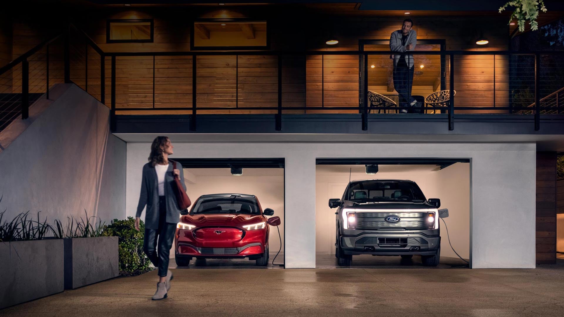 Woman walking out from home garage with a 2024 Mustang® Mach-E and Ford Lightning® truck in plugged-in and charging | Krapohl Ford & Lincoln in Mount Pleasant MI