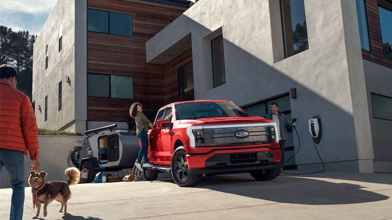A couple talks to a neighbor as one of them unplugs their F-150 Lightning® from a home charging station
